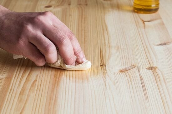 A woodworker applies a high-quality finish to walnut wood in a bright workshop.