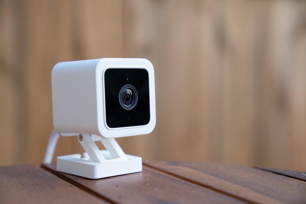 A discreet mini security camera placed on a wooden shelf in a bright home.