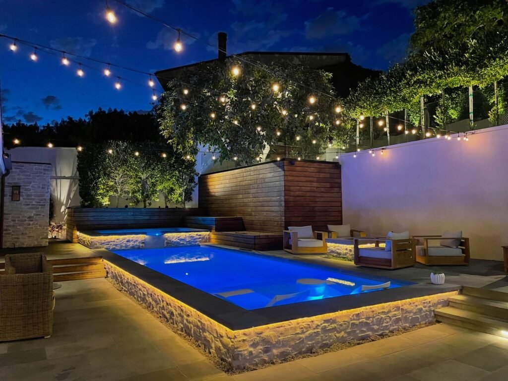 A modern backyard swimming pool glowing with vibrant LED pool lights at dusk.