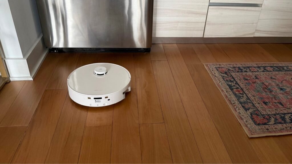 A modern robot vacuum cleaner sits on a polished hardwood floor in a home.