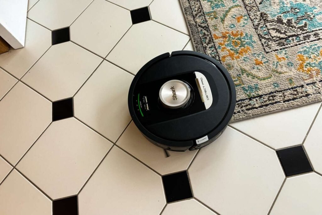 A modern robotic vacuum cleaner sitting on a soft plush carpet in a home.