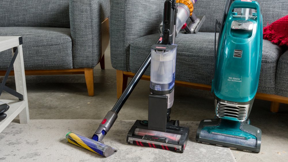 A modern cordless stick vacuum stands in a bright apartment living room.