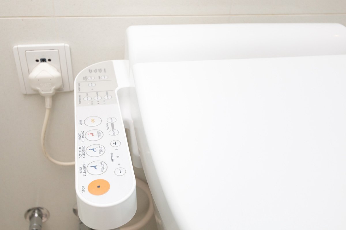 A GFCI outlet plugged into a white bathroom wall near a bidet toilet.