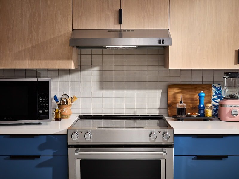 A person performing maintenance by removing the filter from a kitchen range hood.