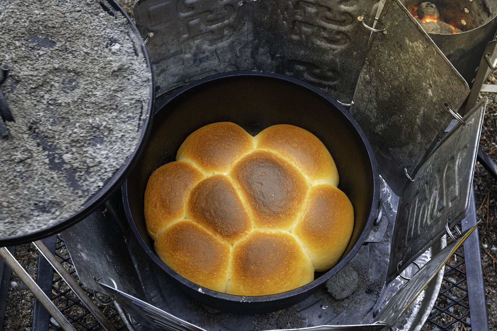 A hiker adjusts a portable camping stove to prepare for bread baking outdoors.