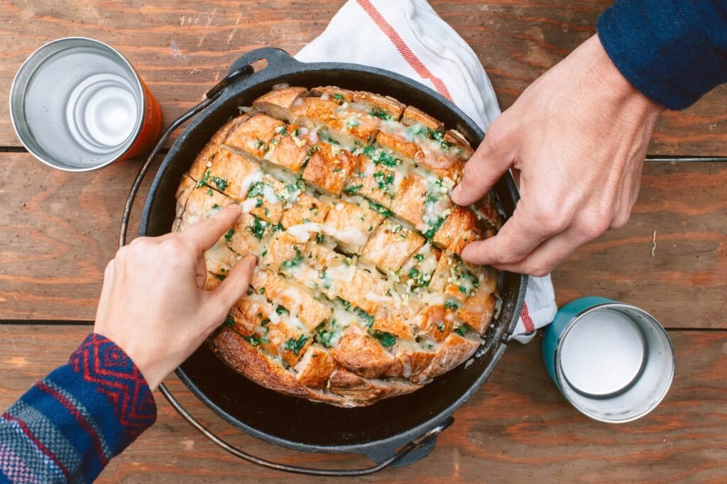A freshly baked loaf of bread sits beside a portable camping oven outdoors.