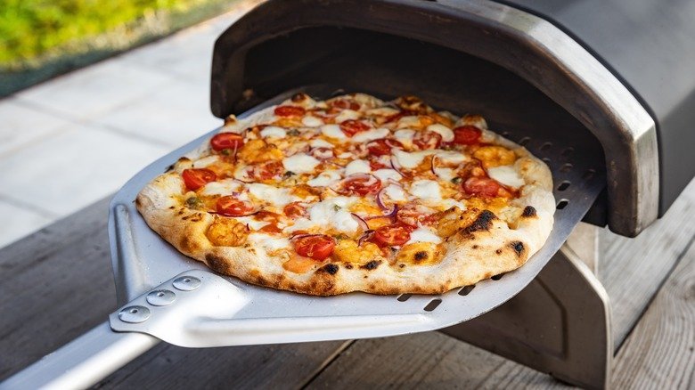 A frozen pizza slides into a hot outdoor wood-fired pizza oven.