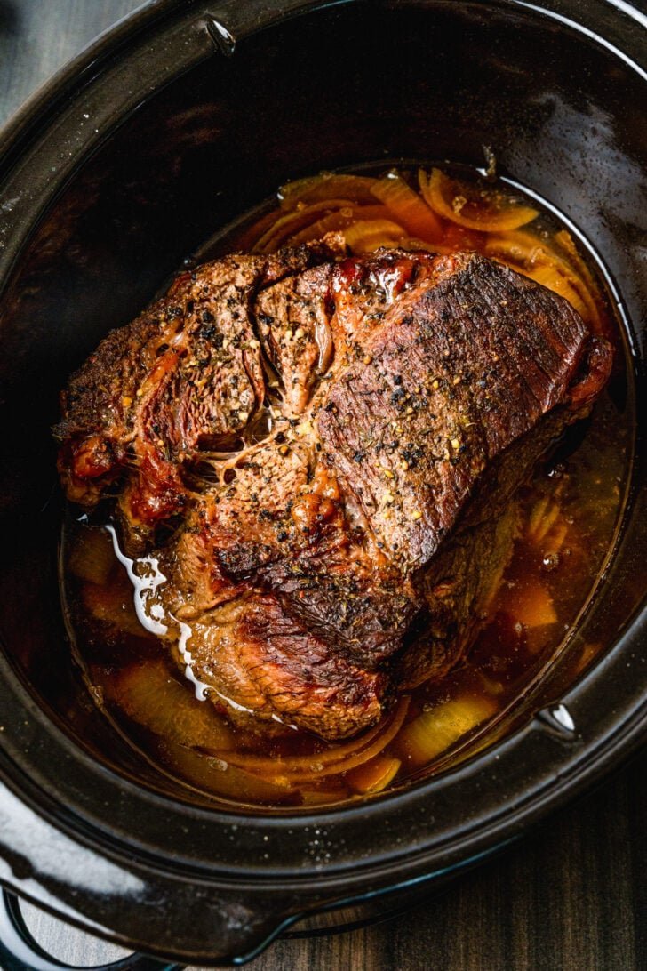 An open recipe book and kitchen tools sit beside a slow cooker on a counter.