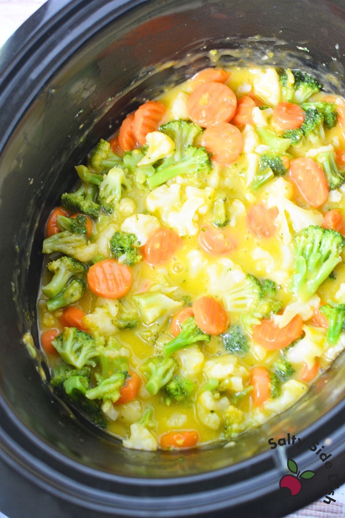 Bowls of frozen vegetables arranged beside a slow cooker for cooking questions.