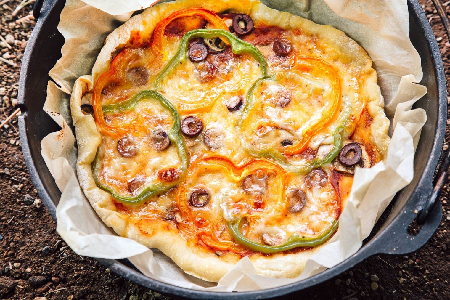 A compact metal camping oven sits on a portable stove at a campsite.
