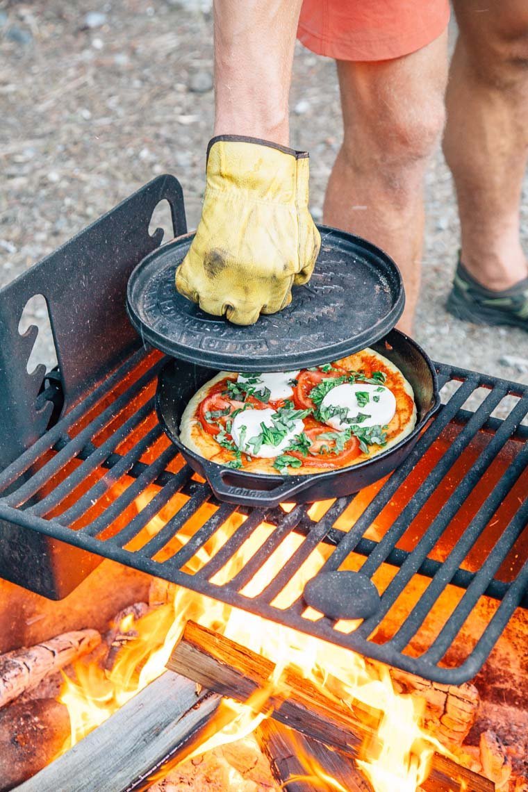 A person carefully cleaning the interior of a metal camping oven after cooking.
