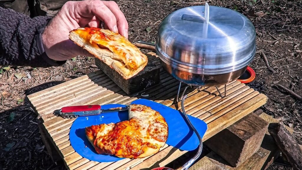 A delicious homemade pizza rests beside a portable camping oven in a forest.