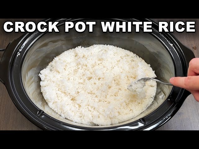 A slow cooker with cooked rice sits on a counter next to kitchen tools.