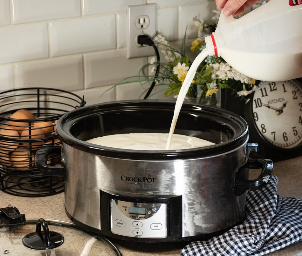 A person checking the temperature of milk in a slow cooker using a digital thermometer.