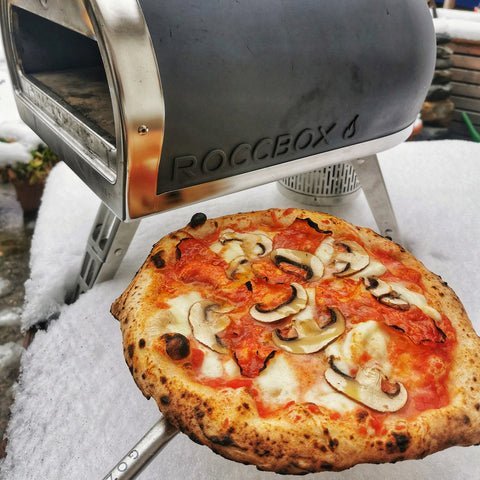 Dry firewood and a thermometer near an outdoor pizza oven for winter cooking.