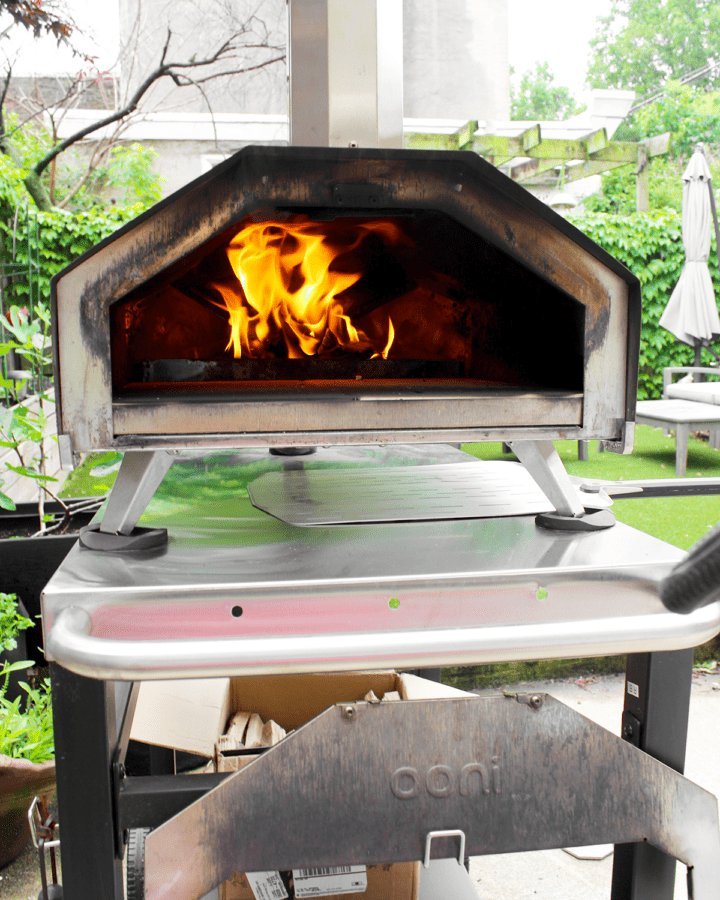 A freshly baked pizza on a peel with a gas oven in background.