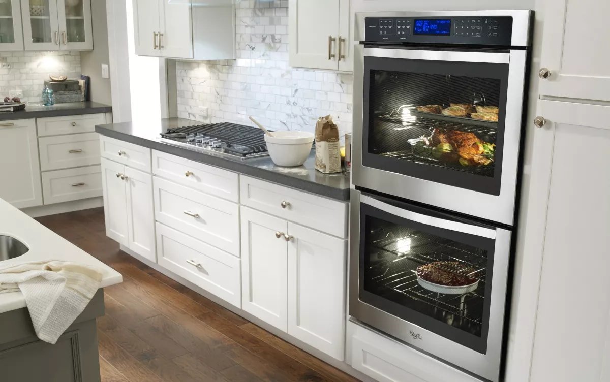 A person repairing the mounting screws of a wall oven installed in cabinetry.