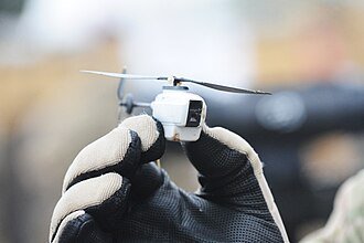 A compact high-definition spy drone hovering in a sunlit backyard garden.