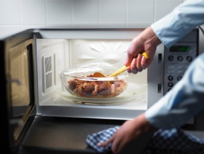 A person stirs food in a glass dish to avoid common microwave heating issues.