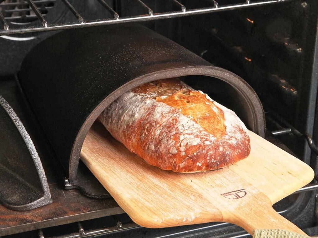 A golden artisan loaf of bread sitting on a wooden board in a kitchen.