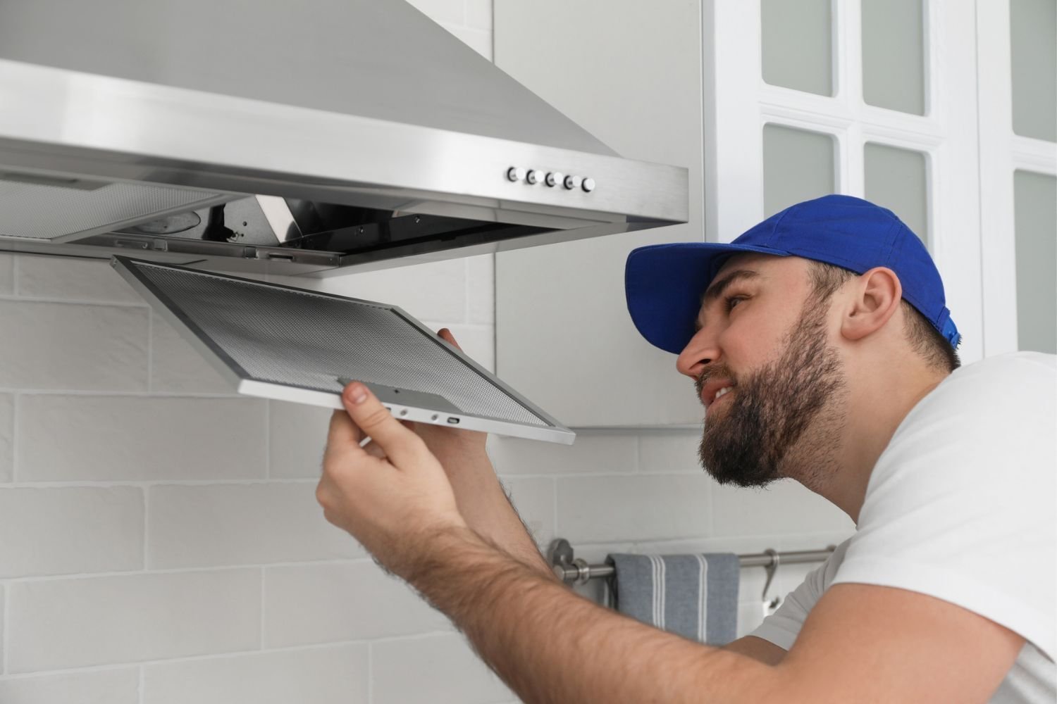Hands removing a metal mesh filter from a range hood for maintenance.