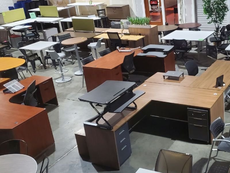 An organized warehouse showroom displaying a variety of high-quality used office furniture pieces.