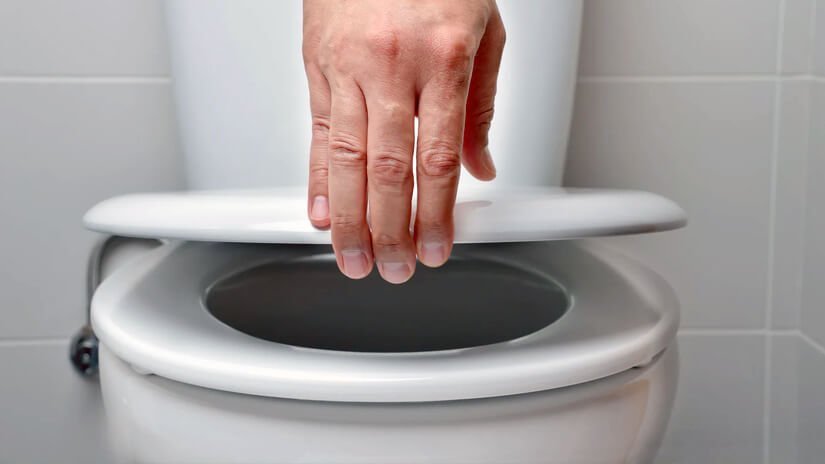 Hands checking for stability on a plastic toilet seat in a bathroom.