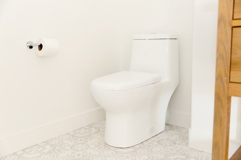 Hands tightening a plastic wingnut under a toilet seat hinge.