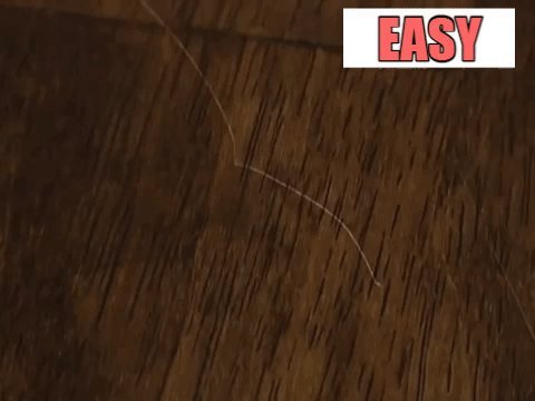A jagged scratch on a polished wooden surface reveals the damaged finish.
