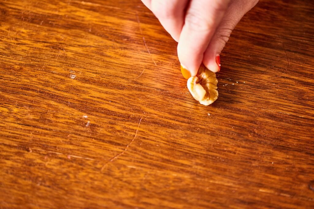 A person repairing a thin scratch on a wooden table with a marker.