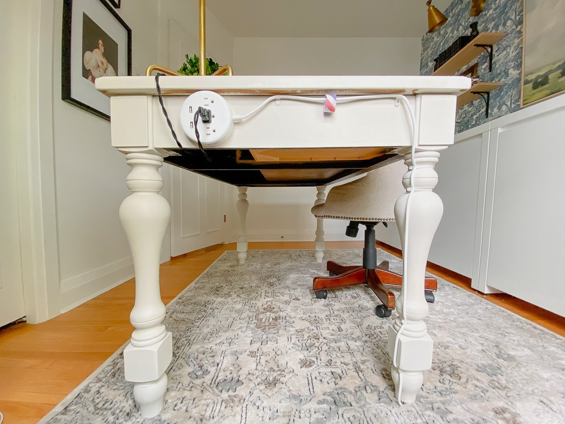 Hands using a cable sleeve to organize messy power cords under a desk.