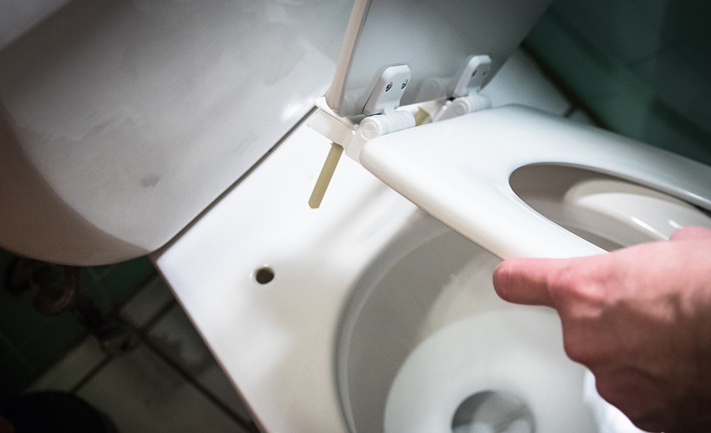 Adjusting the mounting brackets of a toilet seat to fix a loose fit.