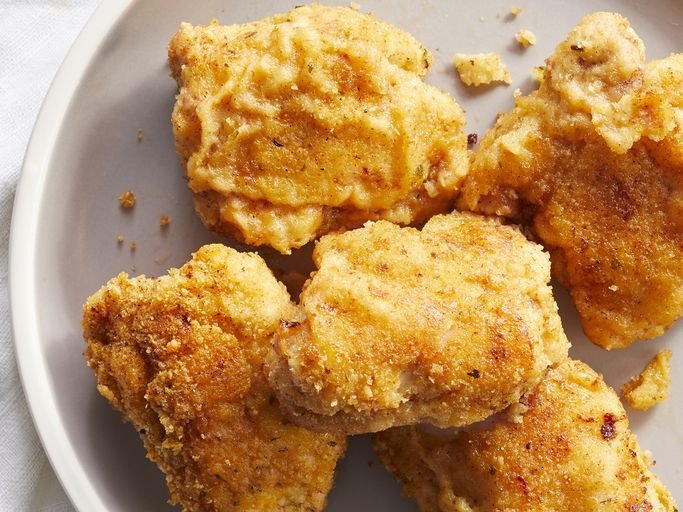 Crispy chicken pieces on a wire rack inside an oven with a thermometer.