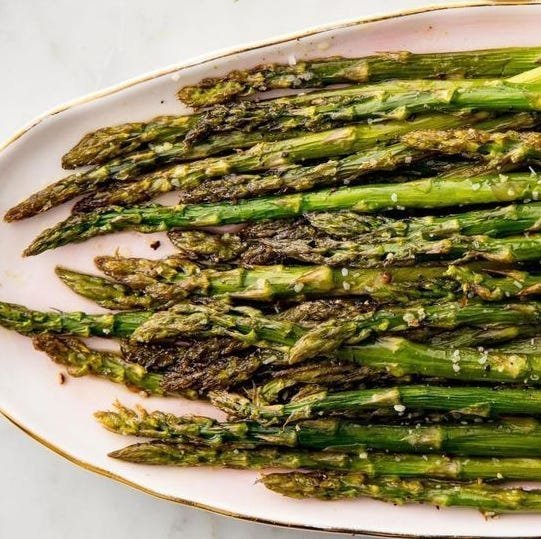 A single roasted asparagus stalk on a plate next to a note-taking pad.
