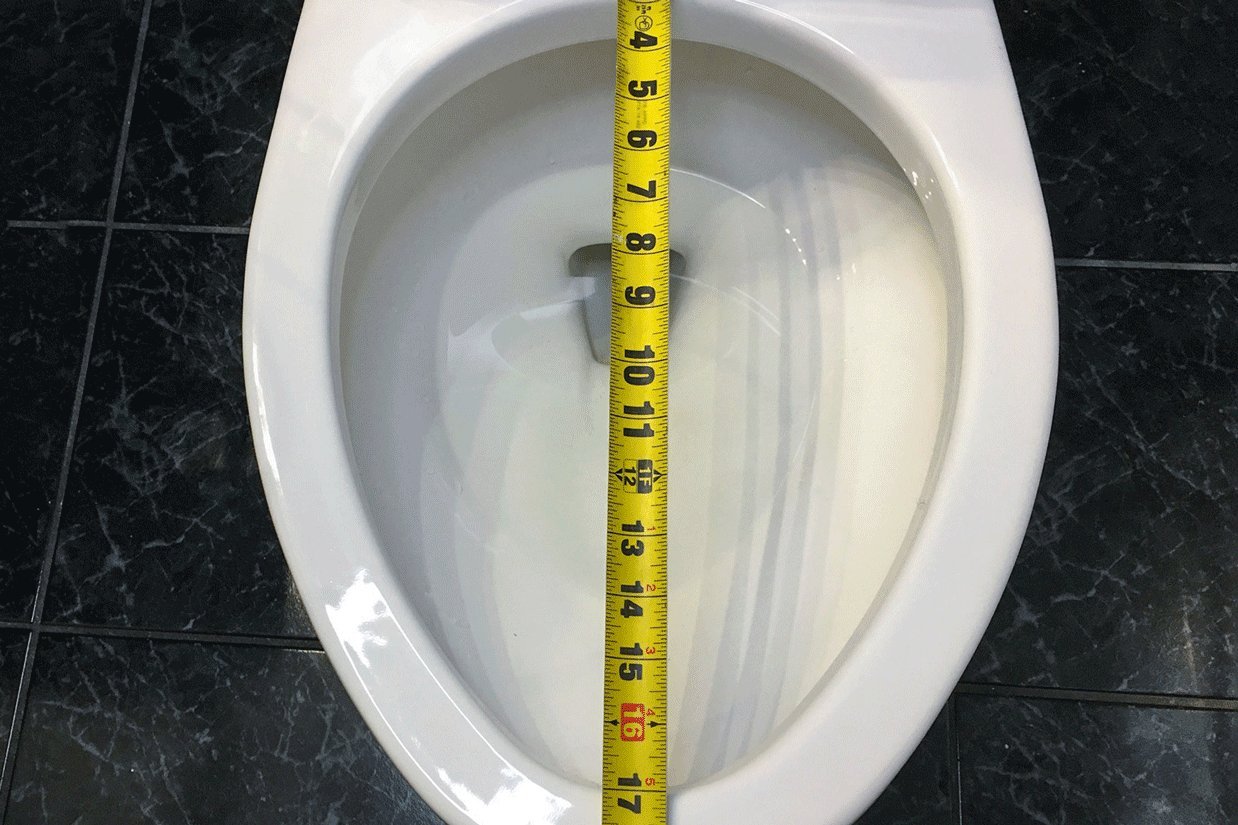 A homeowner prepares to measure a toilet seat for a replacement project.