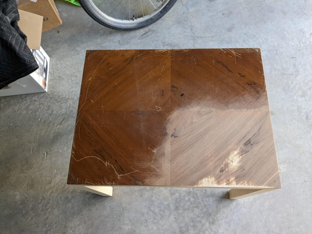 A close-up view of a damaged wooden veneer table top needing repair.