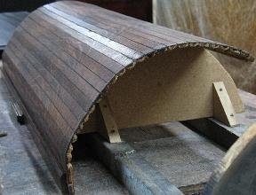 Hands applying glue to repair a loose slat on a tambour door.
