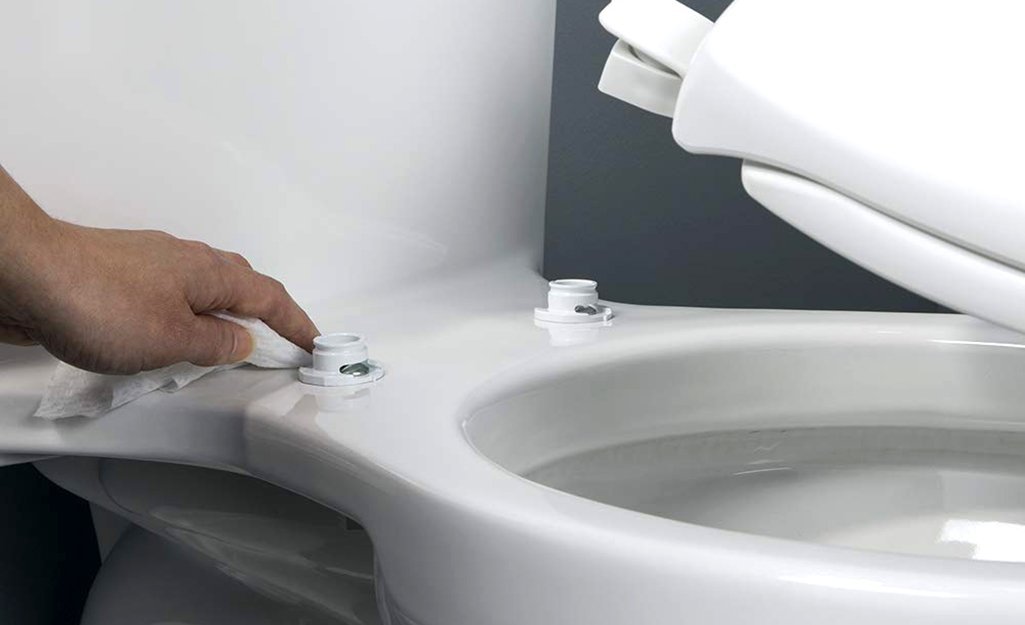 Hands using a screwdriver to tighten hardware on a modern toilet seat.