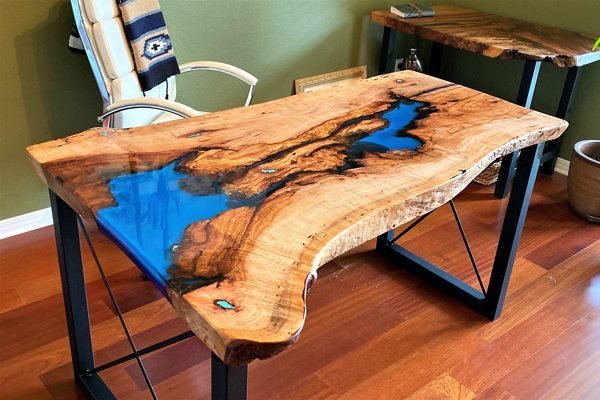 A polished wooden table surface partially coated in clear epoxy resin in a workshop.