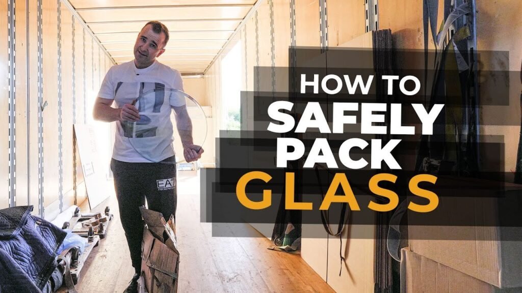 A professional mover carefully transporting a securely wrapped glass table top indoors.