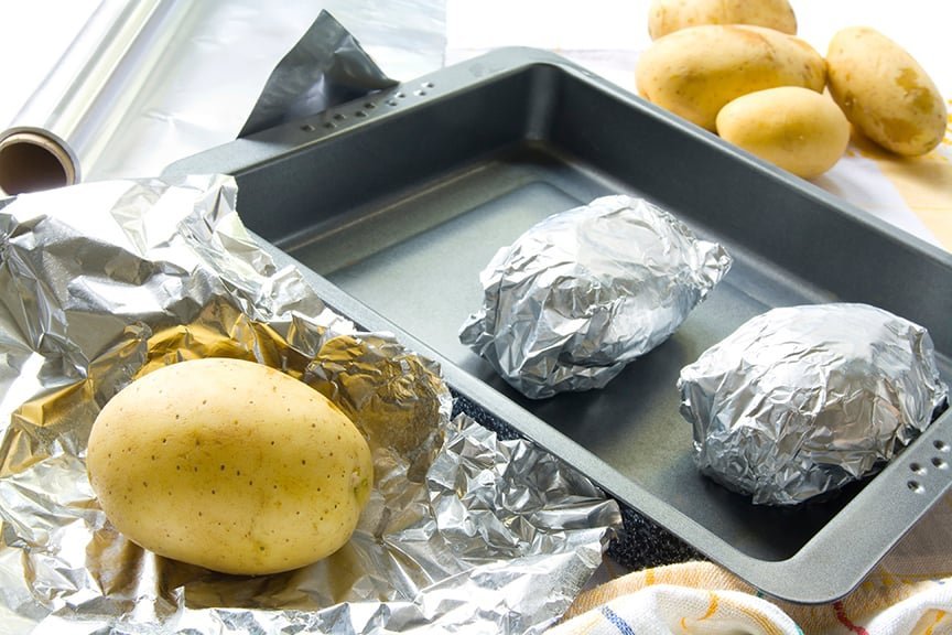 Two potatoes displayed on a counter, one wrapped in foil and one unwrapped.