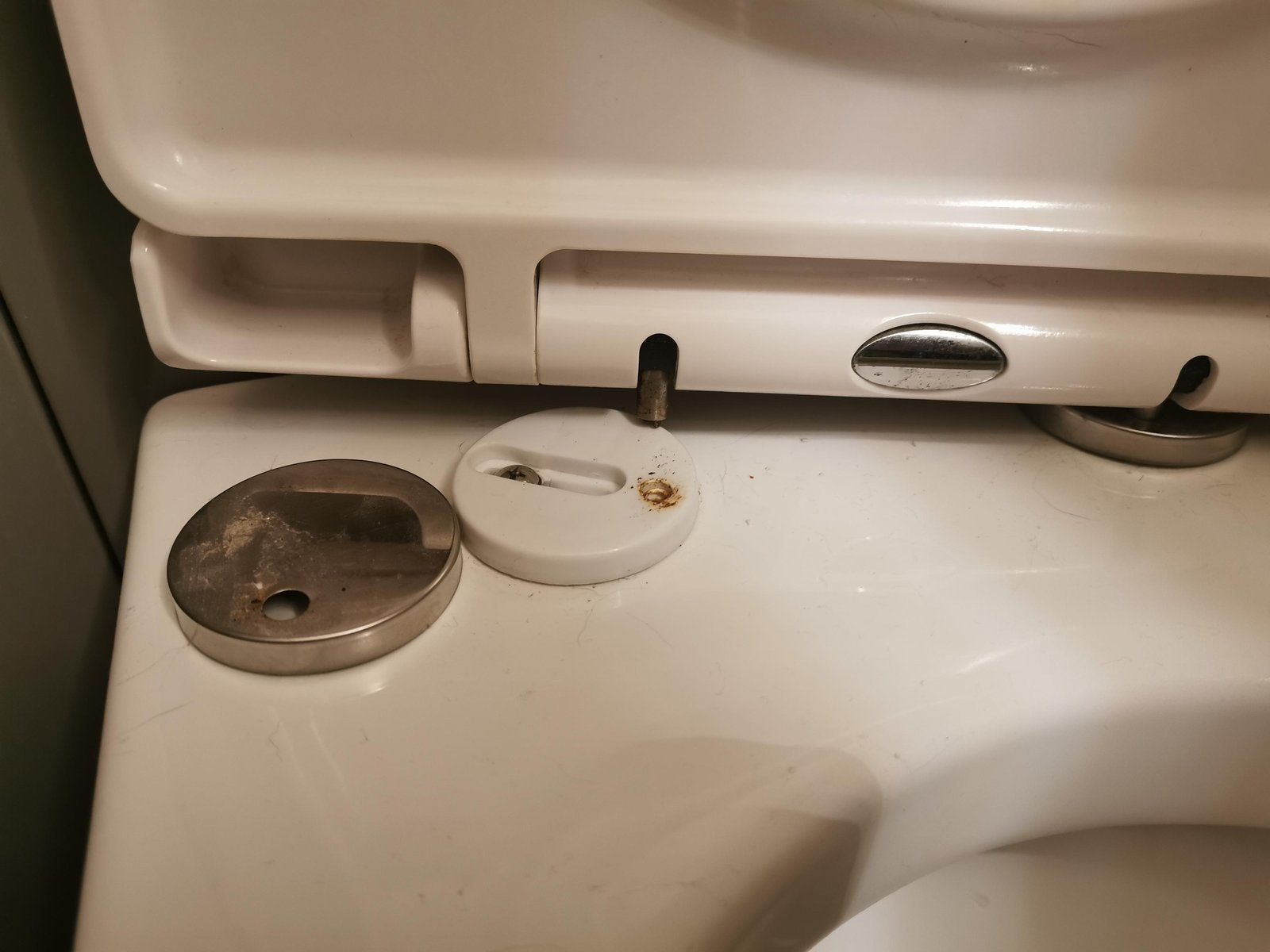Hands repairing a bathroom toilet seat hinge with a screwdriver.