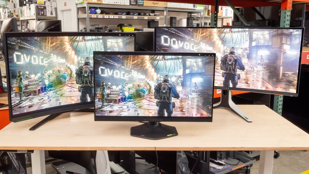 Three gaming monitors of varying sizes arranged on a clean wooden desk.