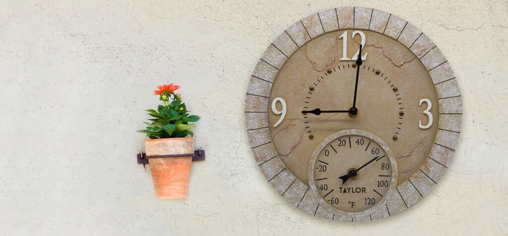A modern outdoor thermometer mounted on a wooden fence in a lush garden.