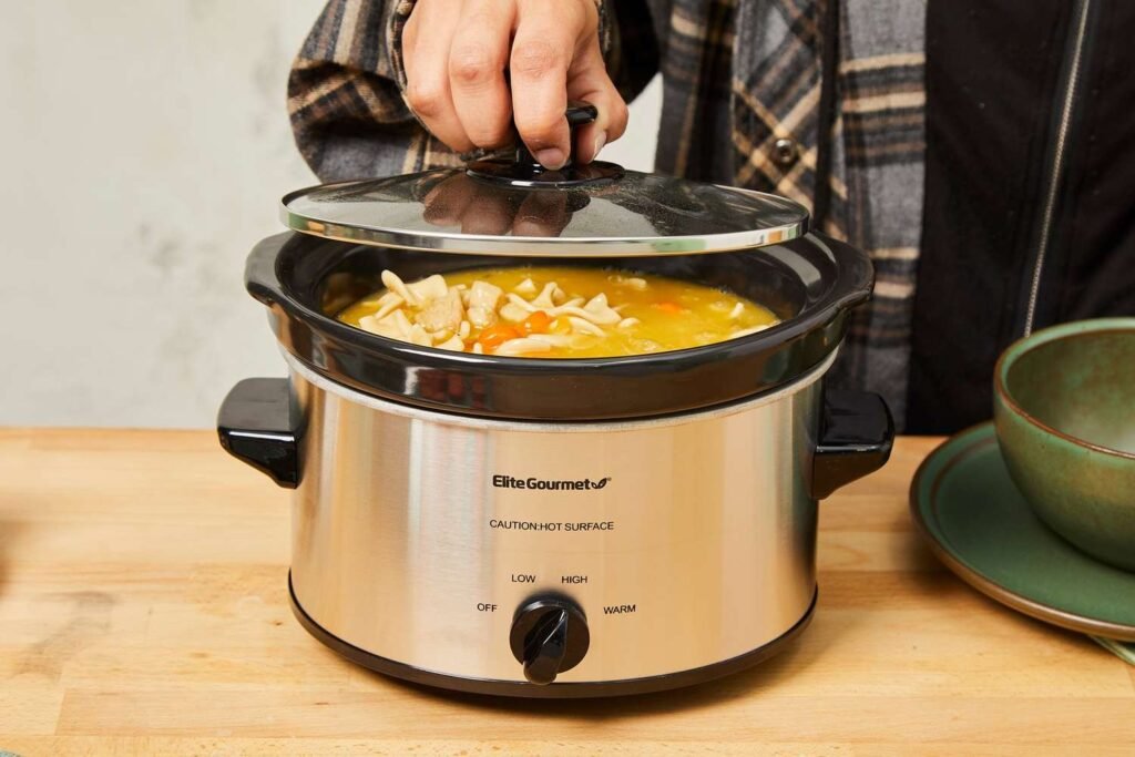 A modern stainless steel slow cooker sits on a marble kitchen counter.