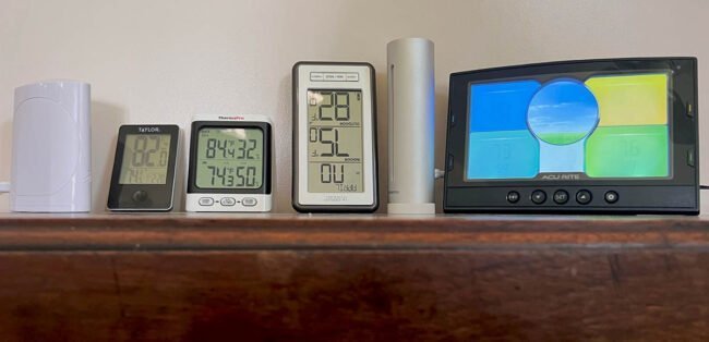 A wireless outdoor thermometer sensor attached to a wooden fence in a garden.