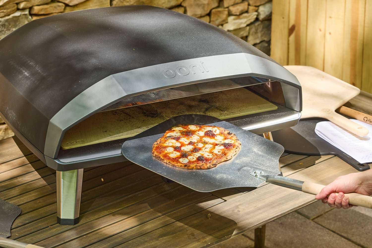 A raw pizza being placed into a high-performance outdoor pizza oven.