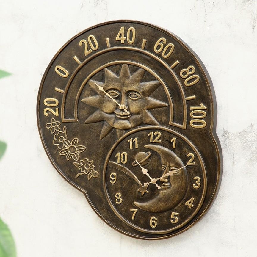 A digital outdoor thermometer mounted on a brick wall in a tidy garden.