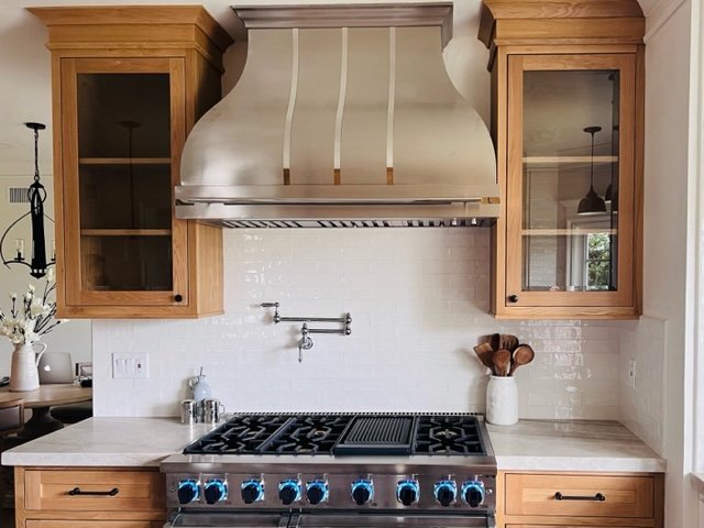 A person carefully cleans the fan blades of a kitchen range hood.