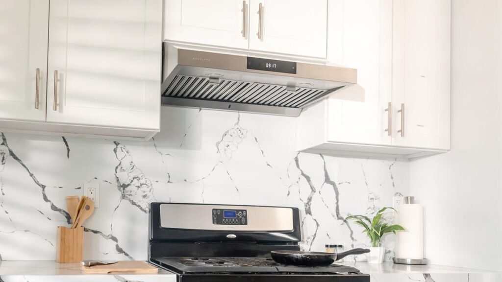 A sleek stainless steel range hood installed in a bright, modern small kitchen.